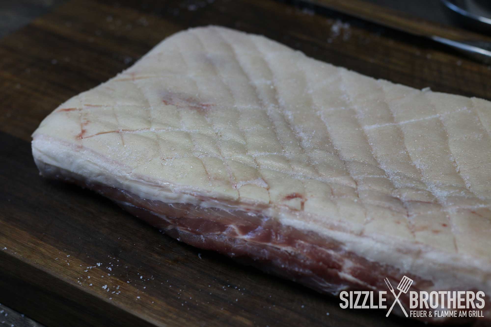 Der Schweinebauch mit eingeritzter Schwarte liegt auf einem Brett