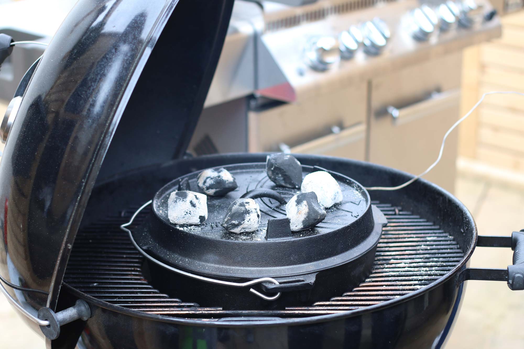 Im Kugelgrill steht ein Dutch Oven mit Briketts auf dem Deckel