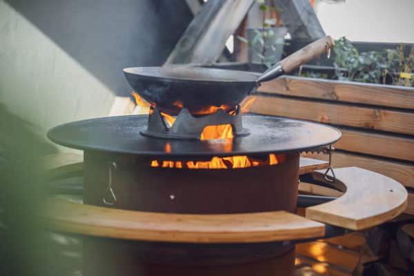 Wok auf einer Feuertonne mit Grillplatte