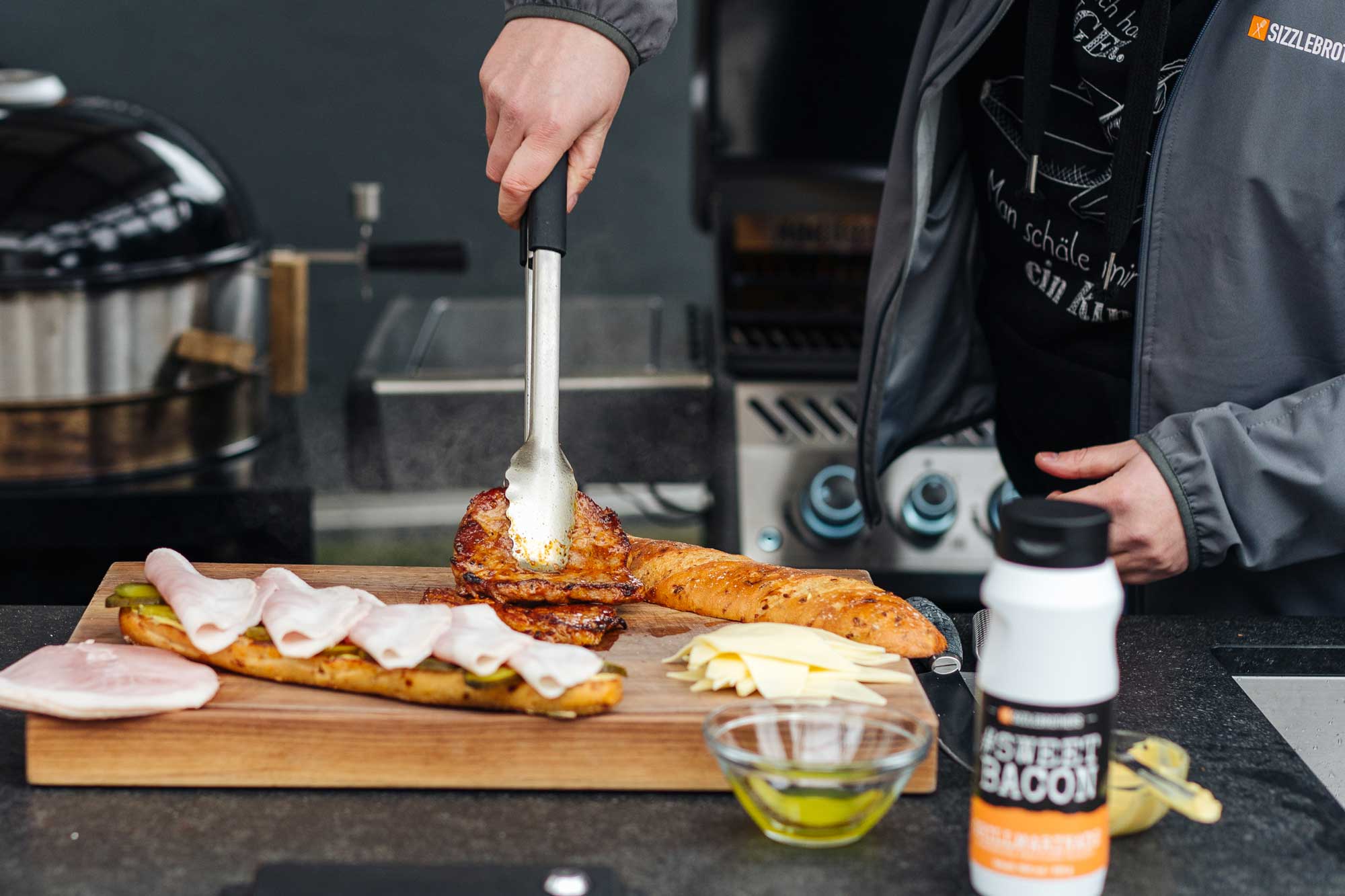 Das Cuban Sandwich liegt auf einem Holzbrett und wird mit den gegrillten Nackensteaks belegt.