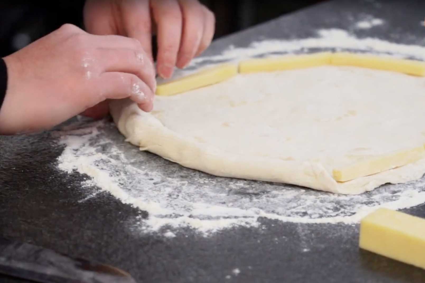 Der hergestellte Teig wird rund geformt und der Rand um die Cheddarstreifen geklappt