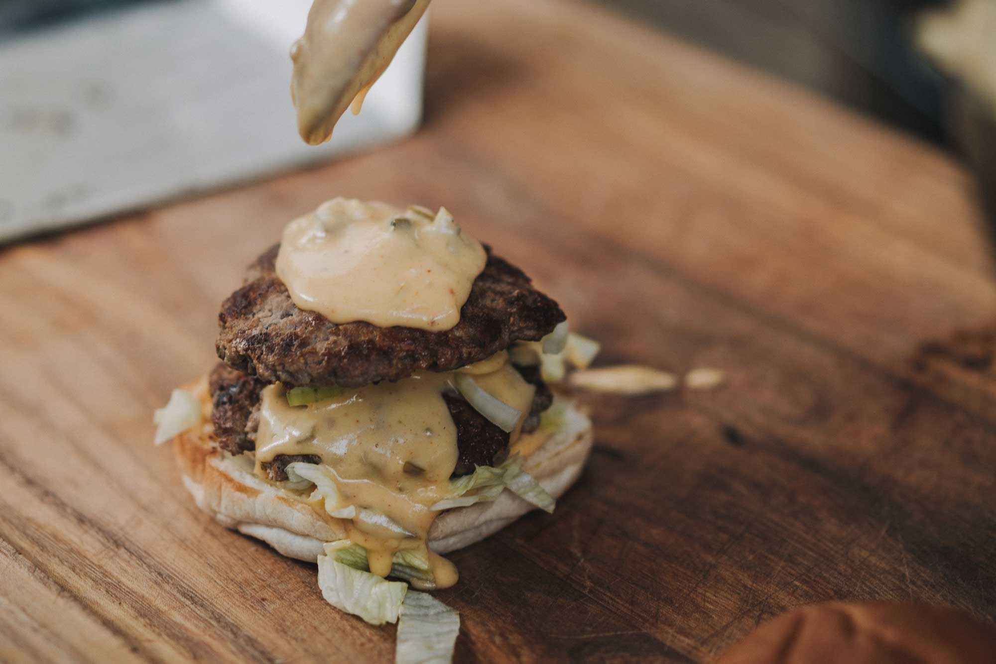 Der Smashed Burger wird großzügig belegt. Unter anderem mit Käsesauce.