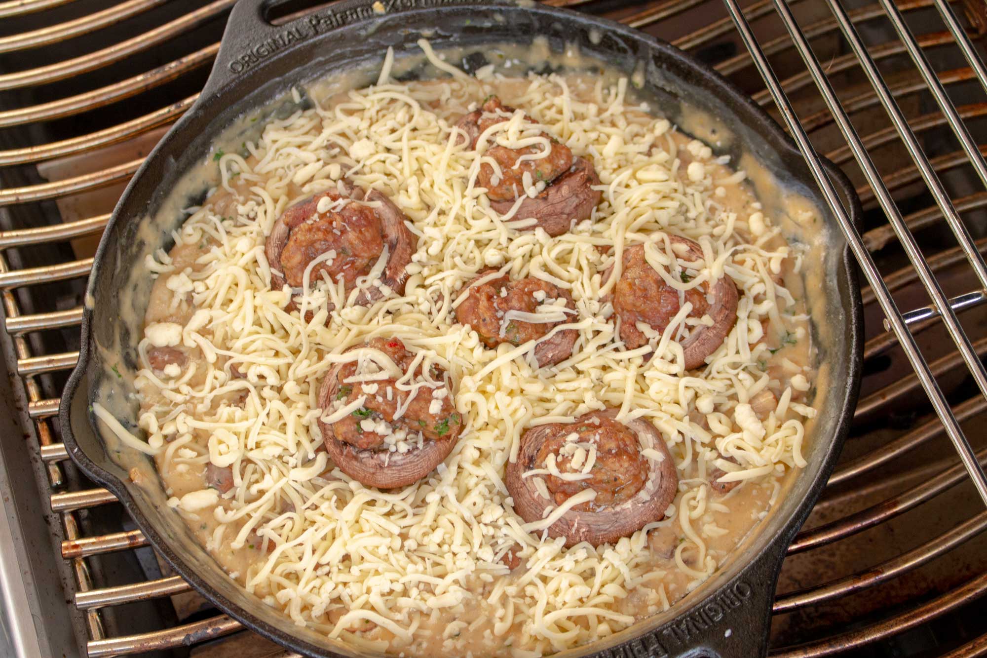 In der Gusspfanne werden die gefüllten Champignons in der Rahmsauce mit Käse gratiniert
