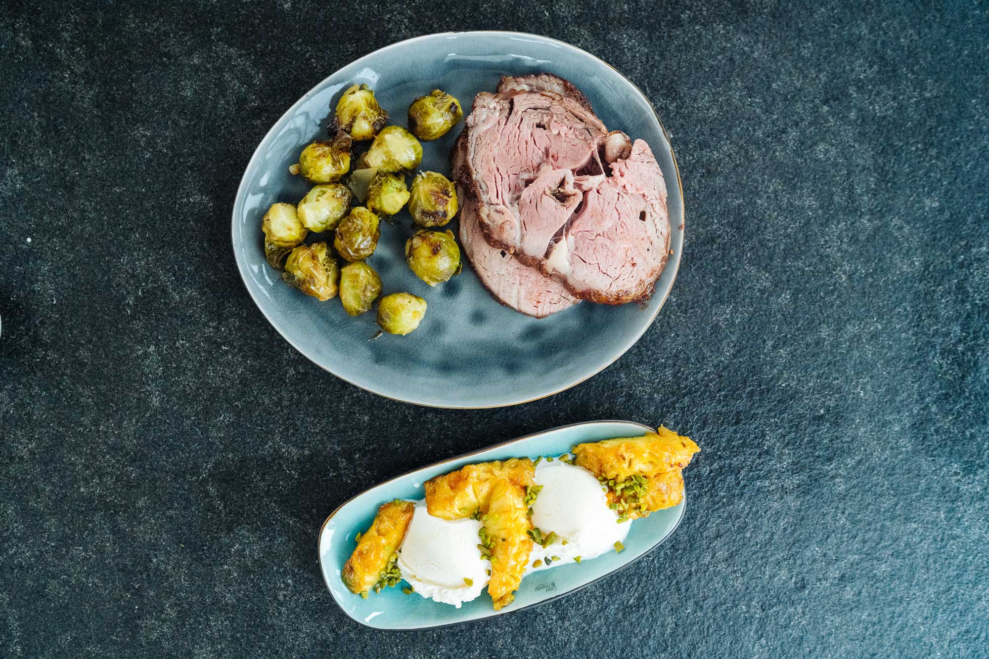 Rib Eye Braten mit Rosenkohl und Karamell Ananas Dessert liegen auf einer dunklen Arbeitsplatte