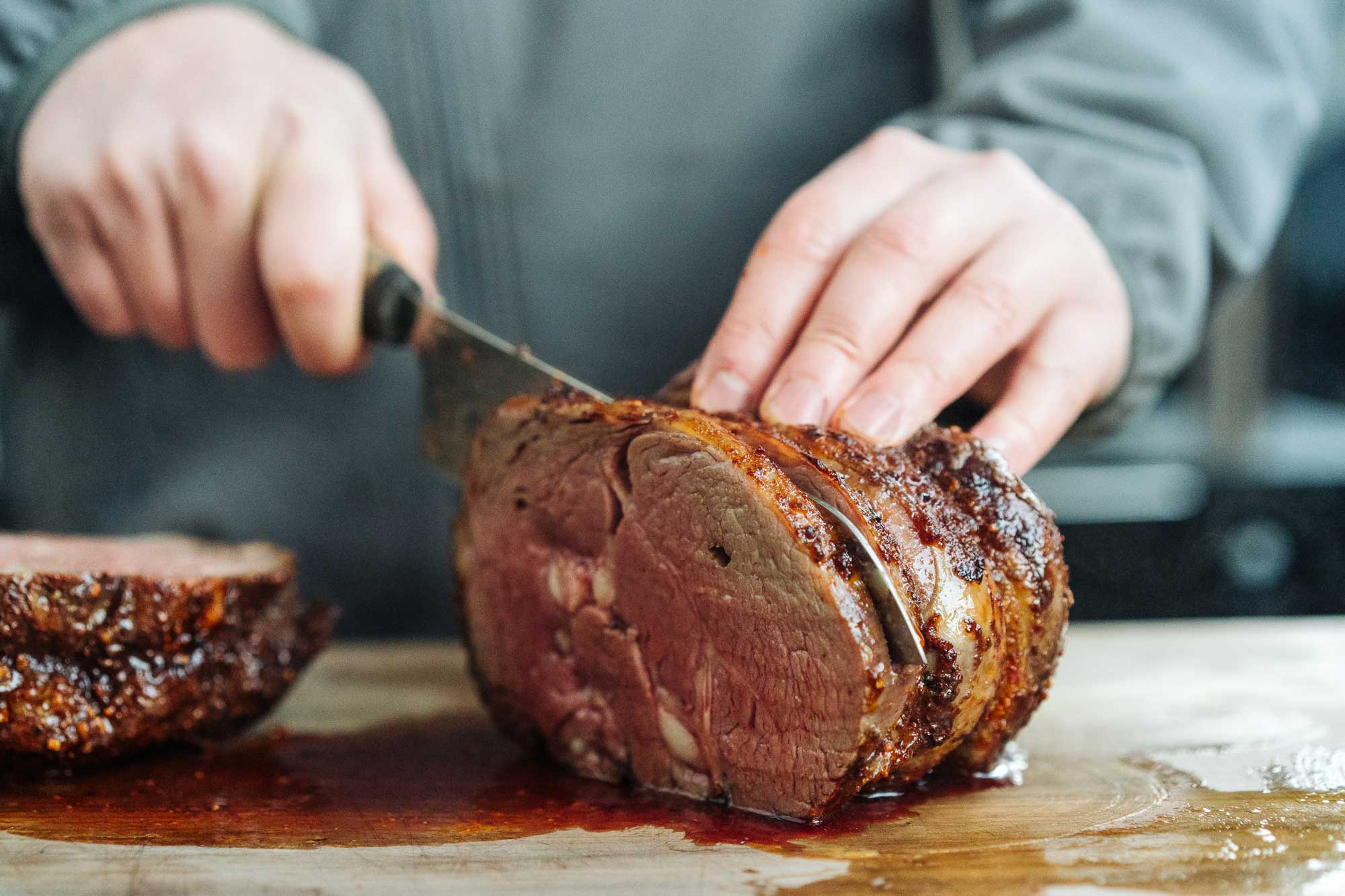 Angeschnitten und zart rosa im Innern liegt der Rib Eye Braten auf einem Holzbrett