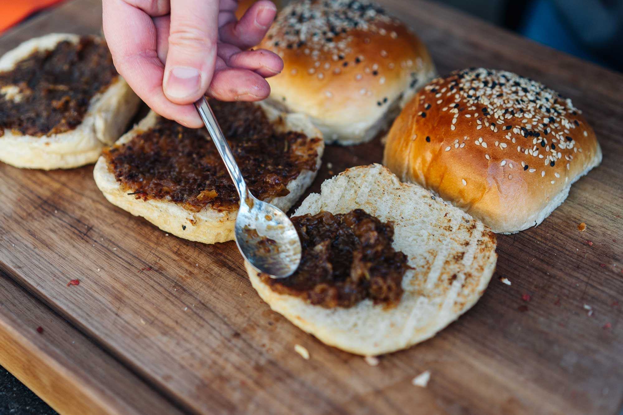 Auf den Brötchen Unterseiten wird Bacon Marmelade verteilt. Sie liegen auf einem Holzbrett