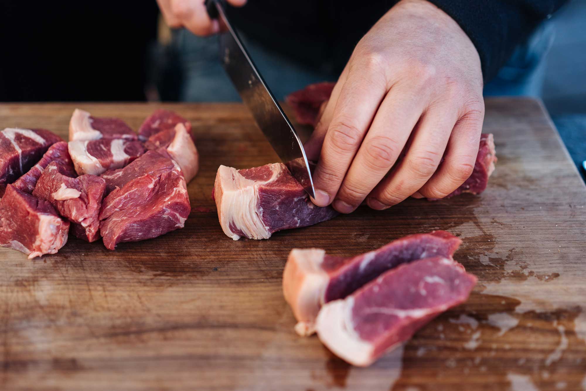 Fleisch wird auf einem Brett in 2 x 2 cm große Stücke geschnitten