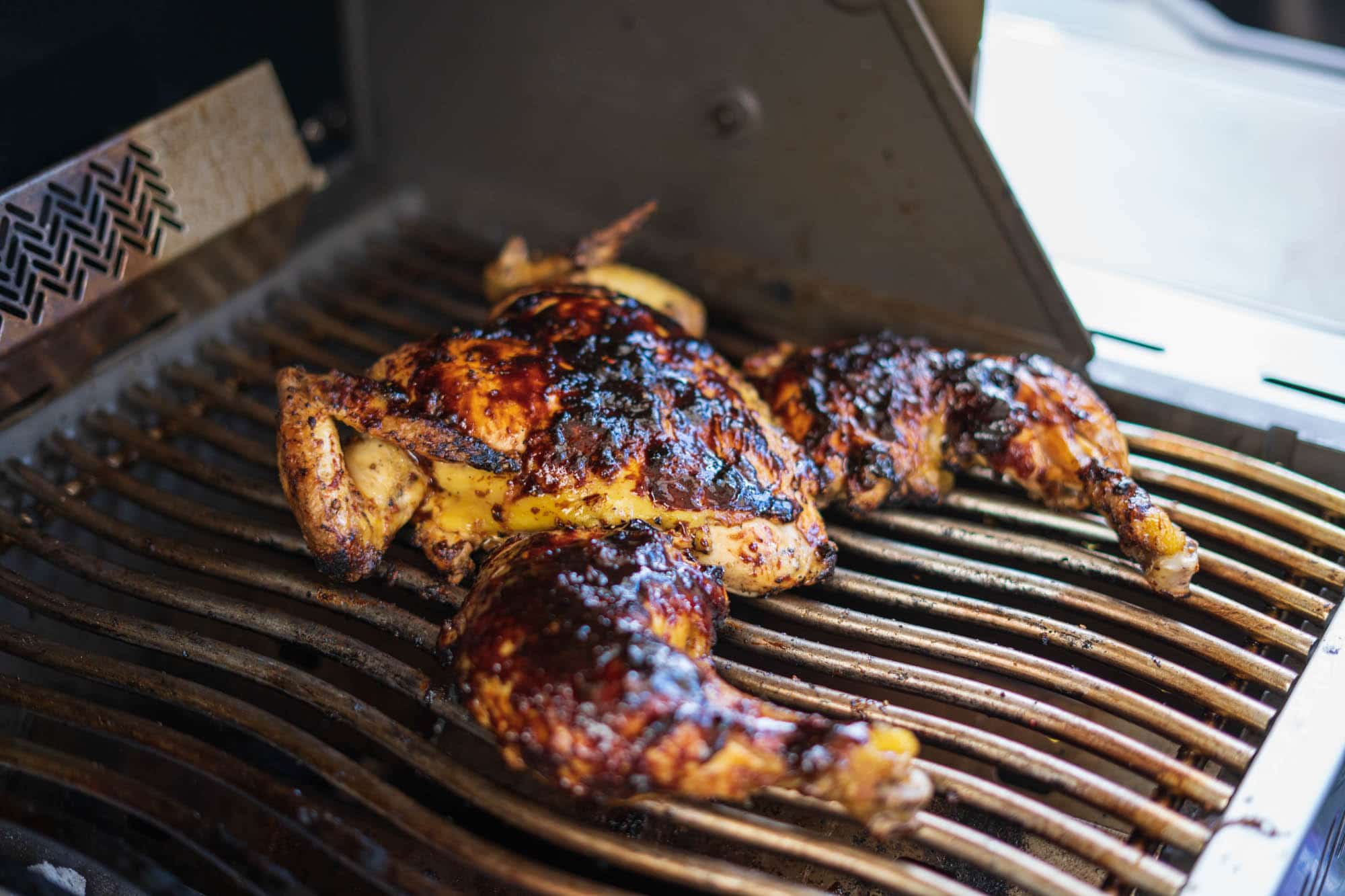 Hähnchen liegt eingestrichen mit BBQ-Sauce auf dem Grill