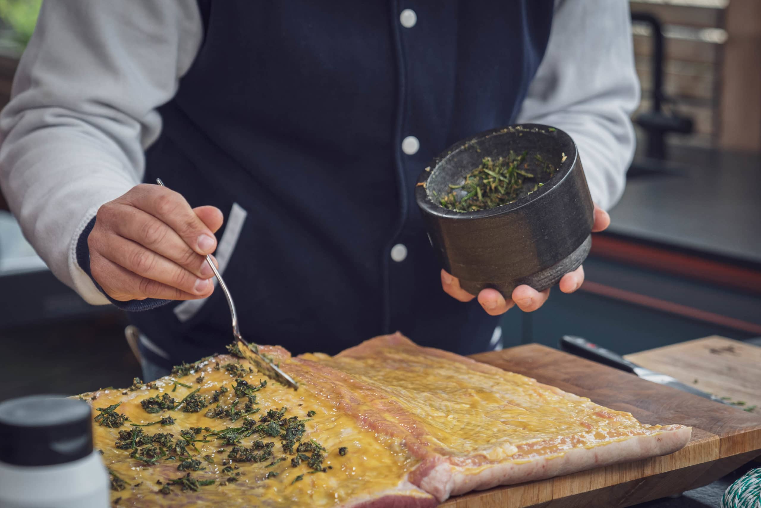Frische Kräuter aus dem Mörser werden auf dem Porchetta verteilt