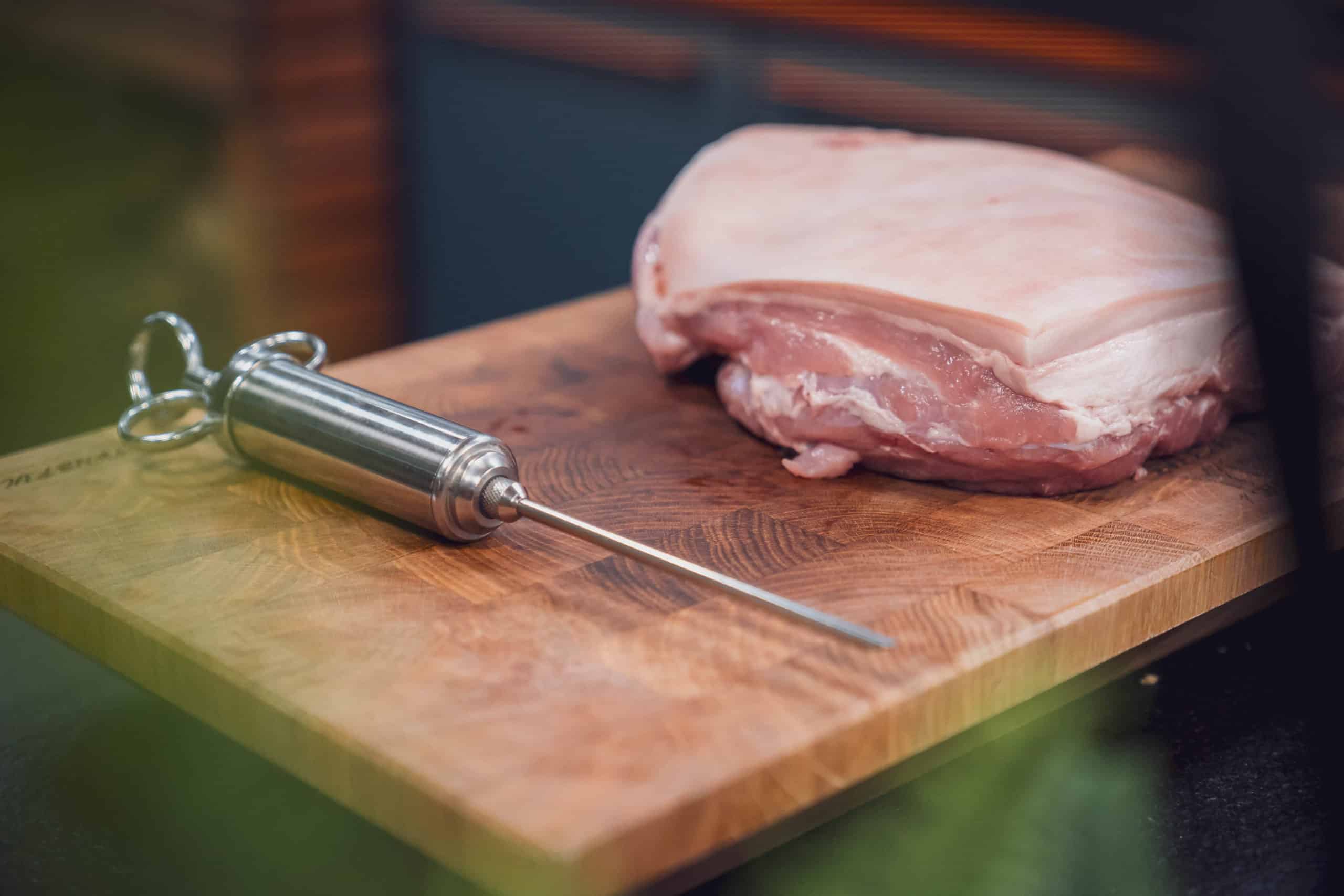 Marinierspritze und Schweinebraten auf einem Brett