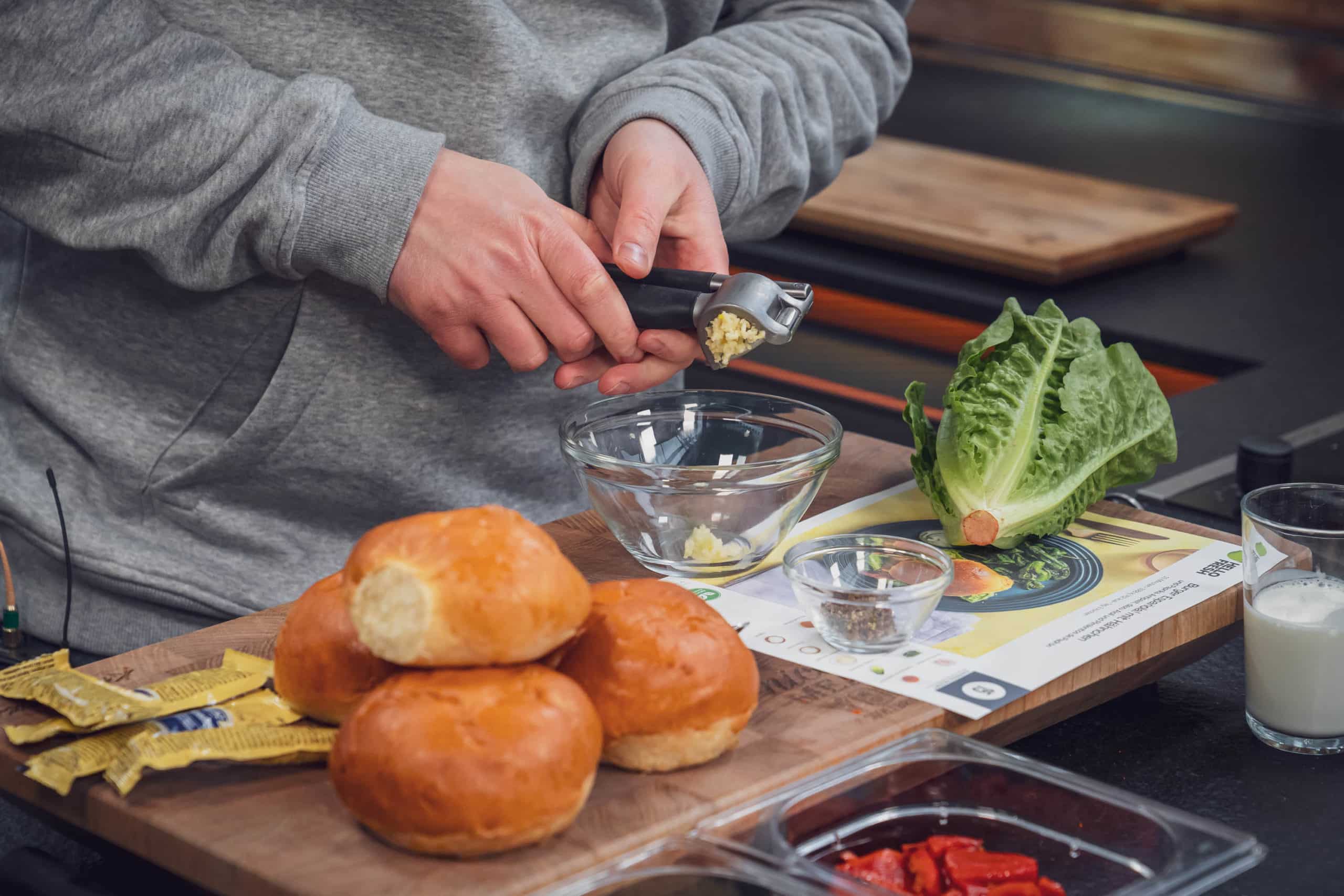 Auf einem Tisch voller Burgerzutaten werden Knoblauchzehen gepresst