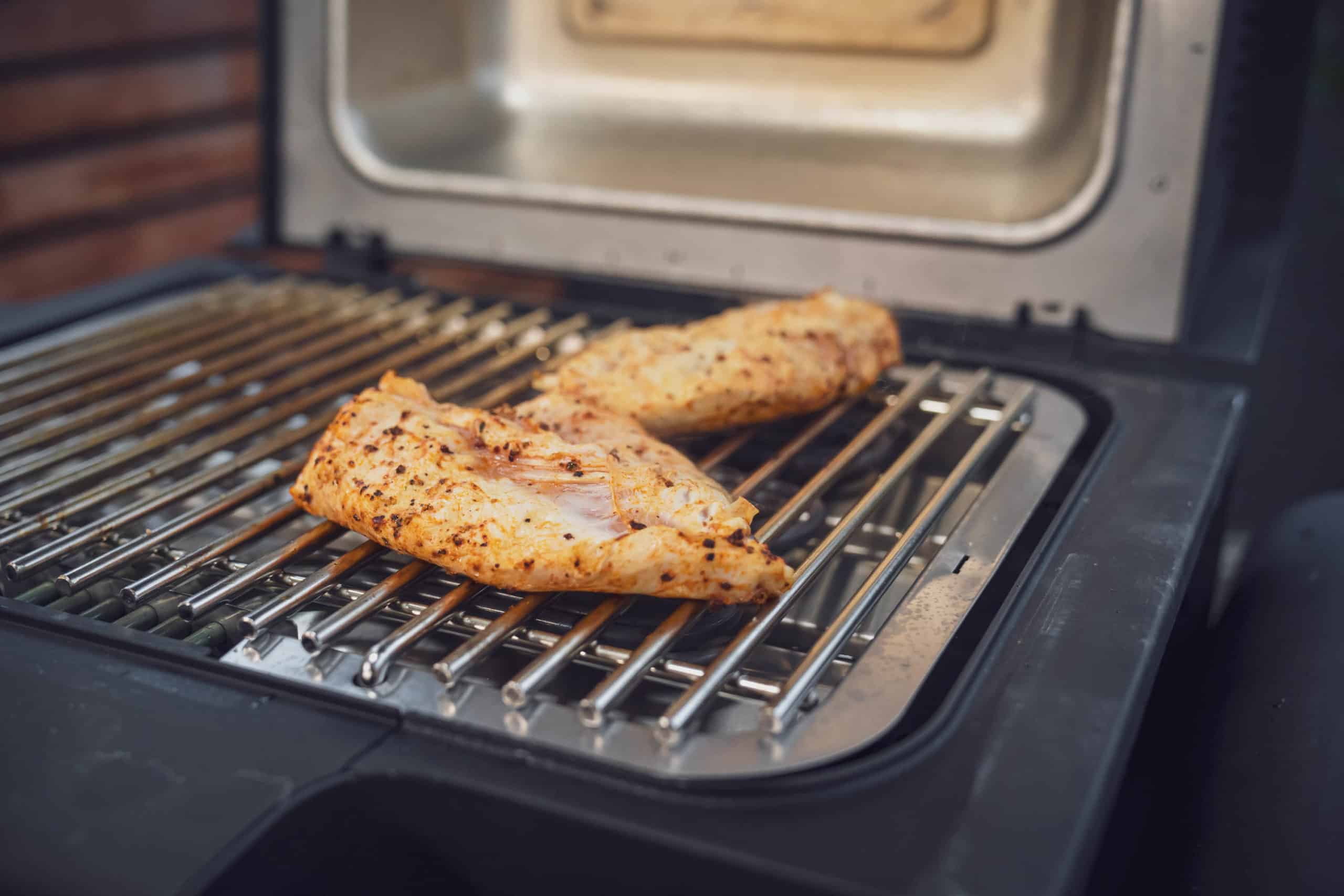 Auf einem Grill werden 2 Hähnchenbrustfilets für Hähnchen Burger gegrillt