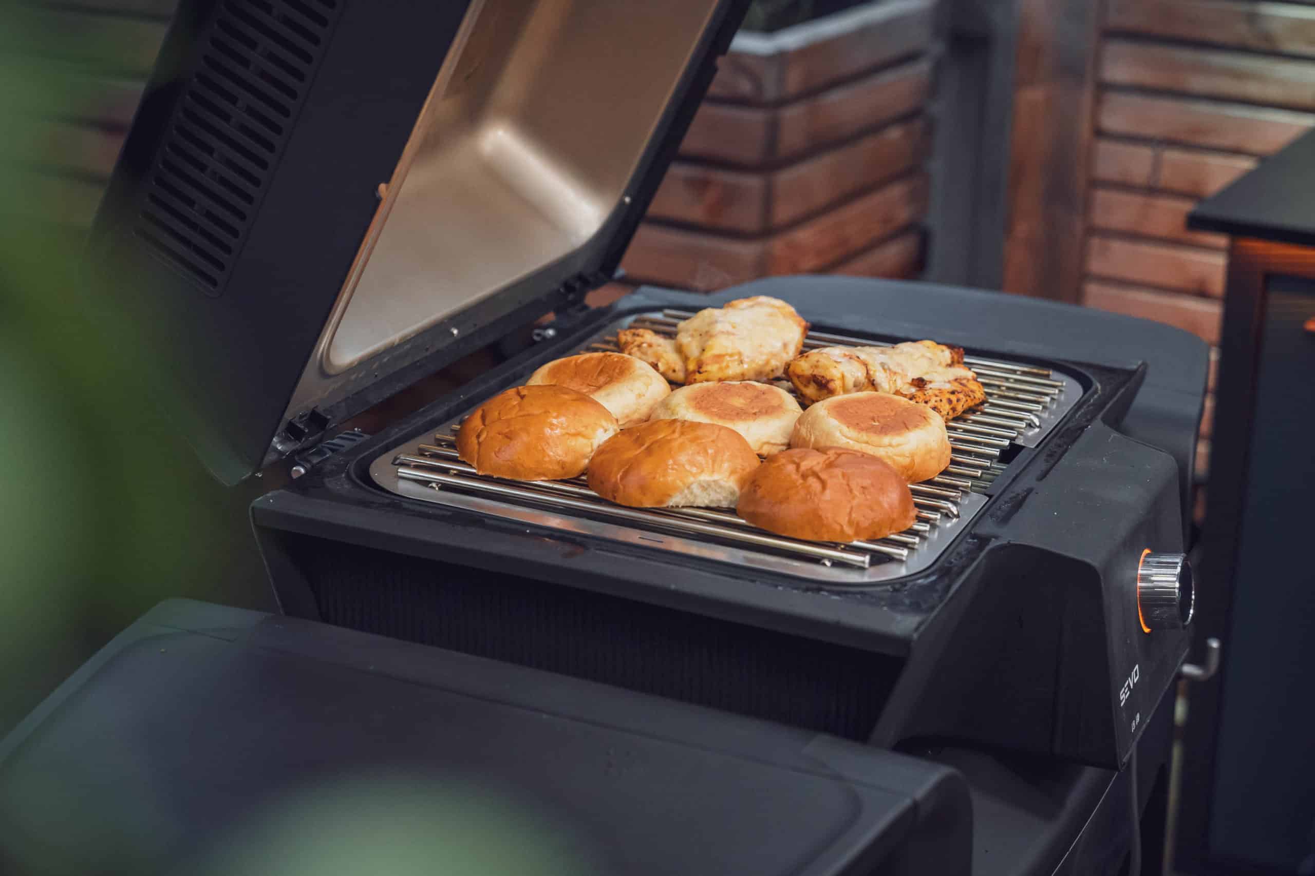 Auf dem Grill liegen Burgerbrötchen und Hähnchenbrust für die Hähnchenburger