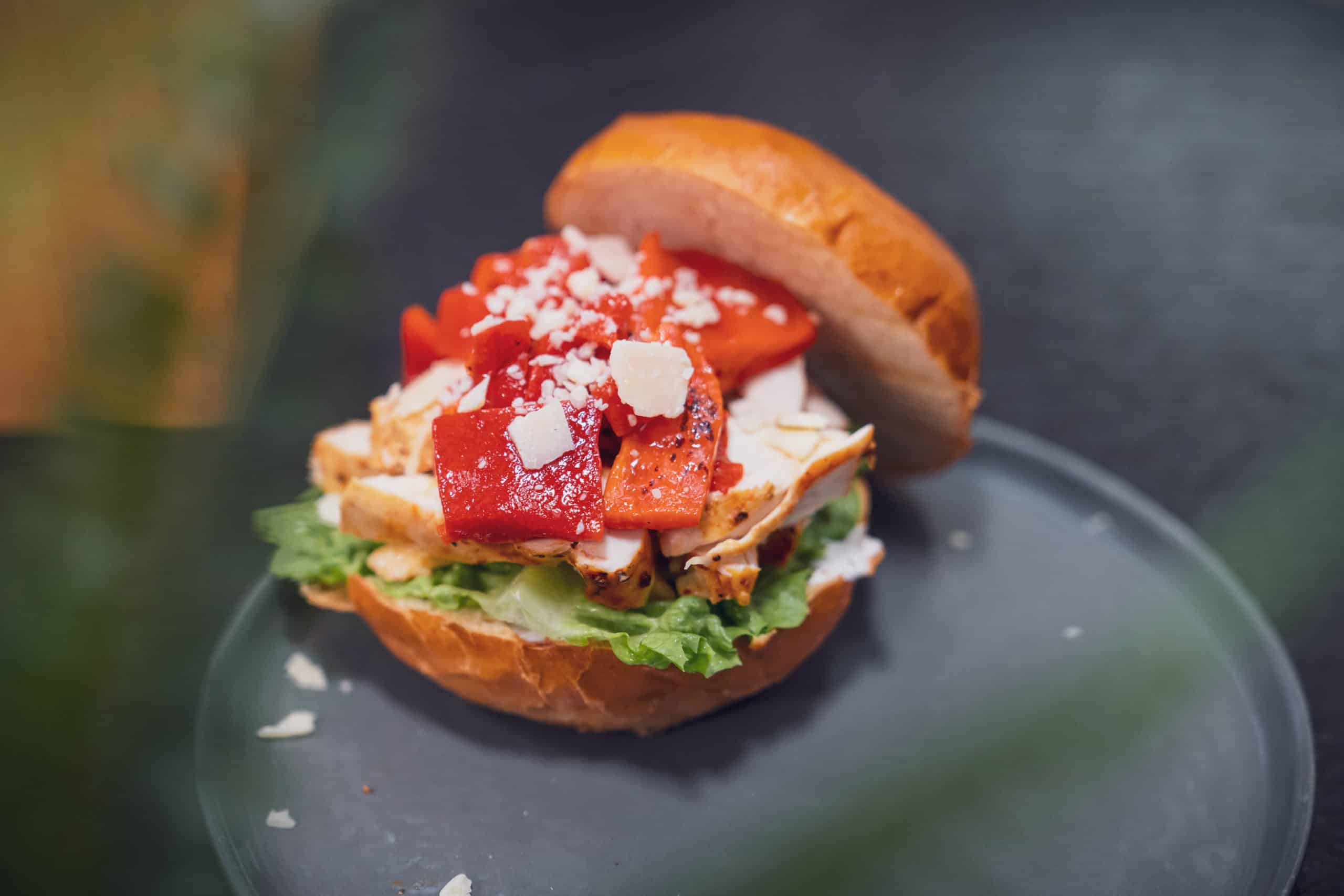 Ein leckerer Hähnchen Burger liegt auf einem grauen Teller