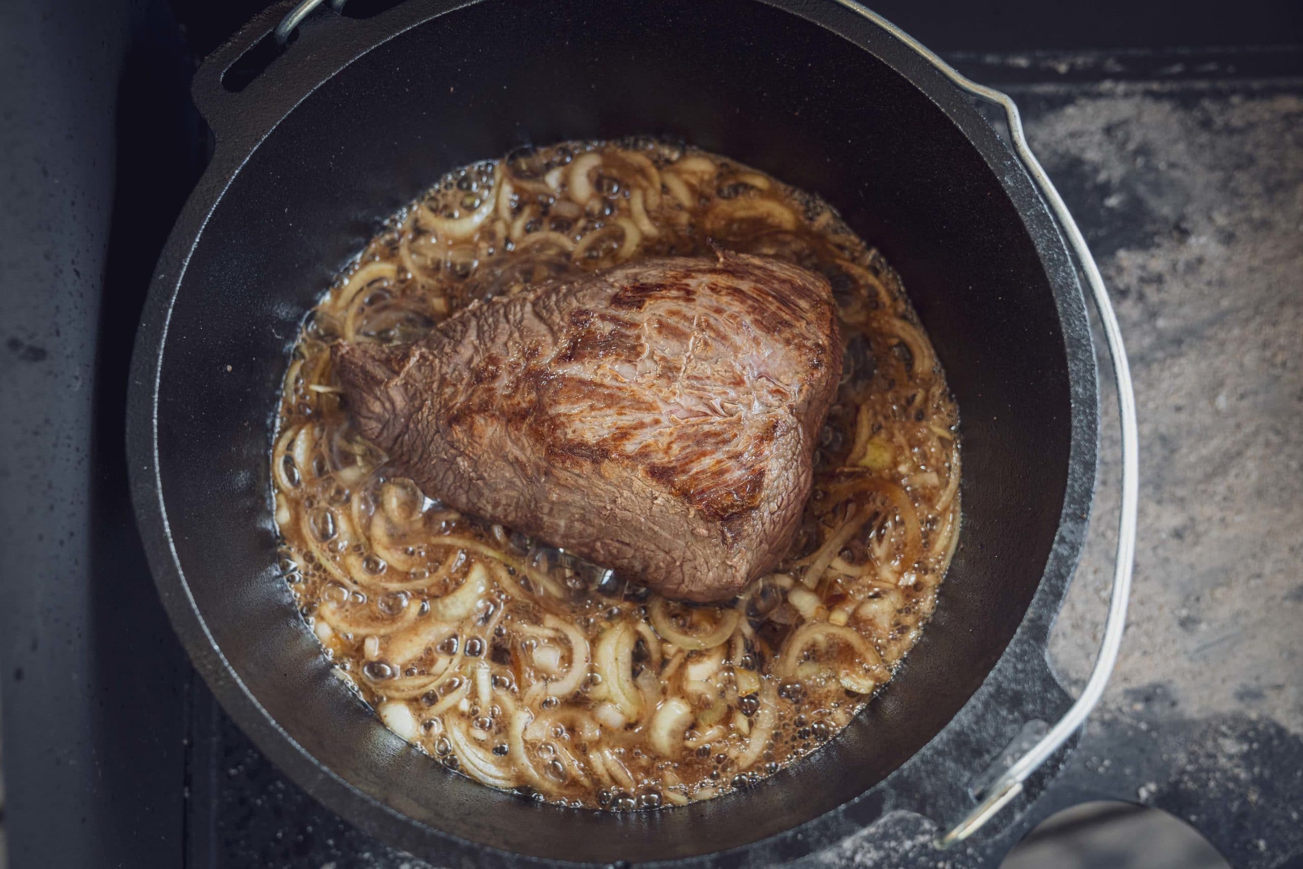 Ein Rinderbraten wird mit Zwiebeln im Dutch Oven geschmort